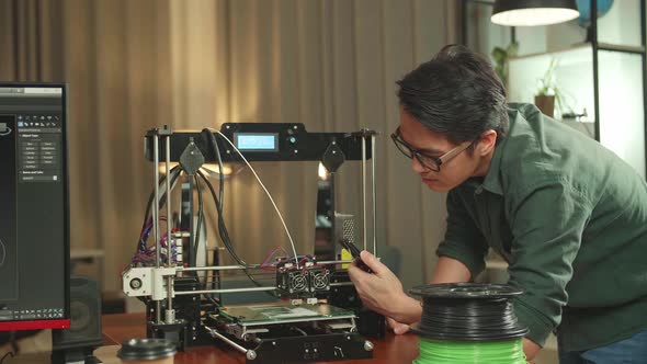 Asian Engineer Using Mobile Phone While Work On 3D Printer Printing And Personal Computer