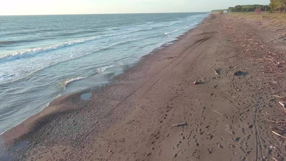 A drone quickly flies over a beach littered with branches and debris after storm