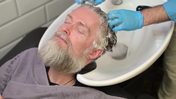 Shampooing before a haircut in a barbershop. Master washes the head of a man