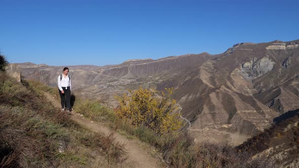 Happy Woman with Backpack Walks Along Track Against Hills