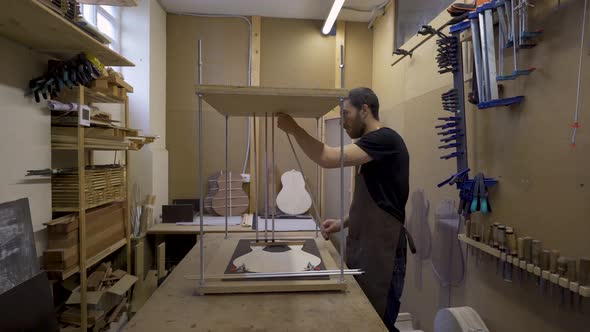 Craftsman installing metal sticks while building guitar in workroom