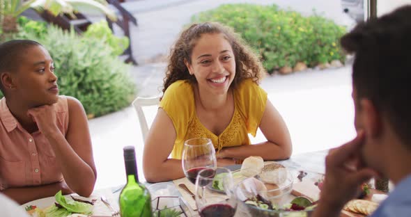 Happy biracial woman laughing with friends at dinner party on patio