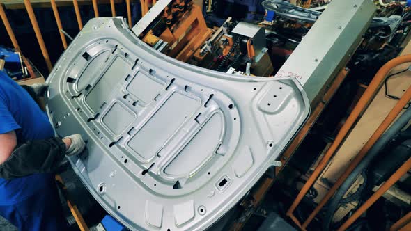 Car Mechanic Assembling a Car Hood at a Car Production Factory