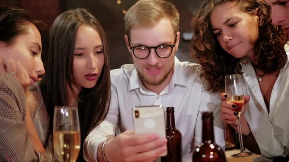 Company of Focused Hipster Friends Using Smart Phone in the Bar, Pub While Caucasian Man Start
