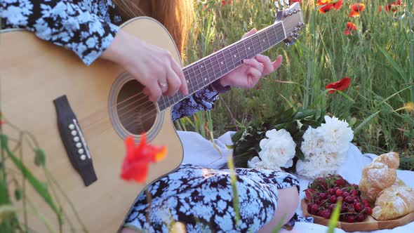 Young woman playing guitar at sunset in a field of flowers in summer. People, relaxation, lifestyle.