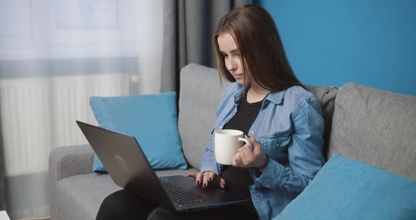Pretty Young Lady Relaxing at Home with Laptop and Coffee