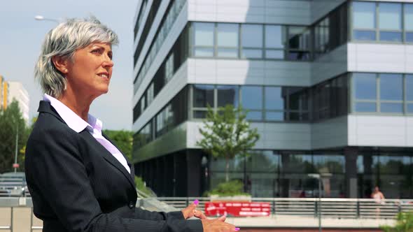 Business Middle Age Woman Looks Around - Company Building in the Background - Shot From Side