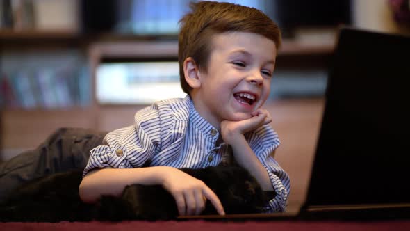 Funny Child with Kitten Using a Laptop at Home.