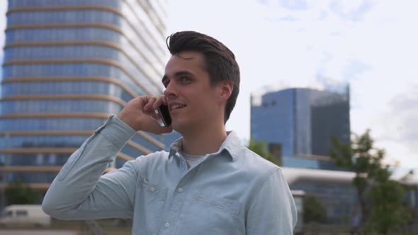 Handsome young man speaks on the phone against the background of a modern city