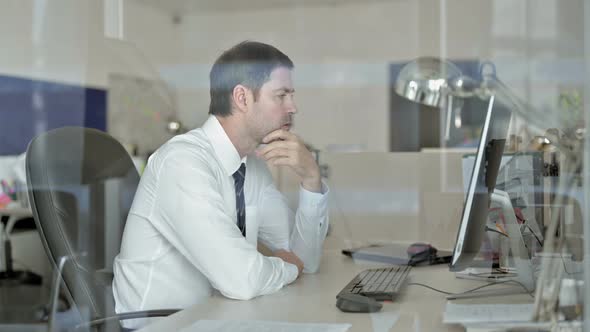 Middle Aged Businessman Thinking and Looking at Computer Screen