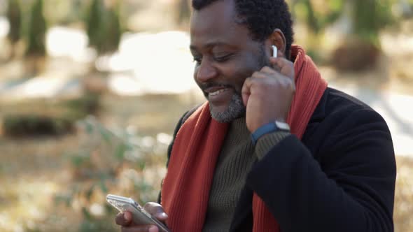 Cheerful African man in headphones listening music in park