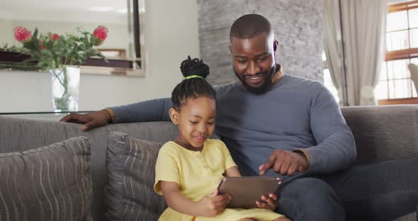 Happy african american daughter and father using tablet on sofa