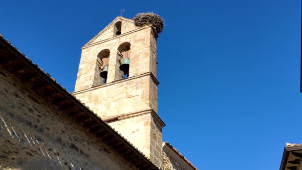 Old church stone tower with a bright deep blue clear sky behind. There are two big bell high on the
