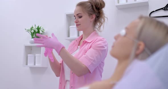 Female Beautician Puts on Gloves Before a Cosmetic Procedure