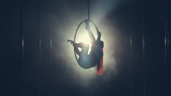 Silhouette of a Gymnast Sitting and Rotating in a Hoop