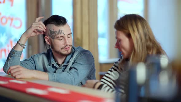 Handsome Tattooed Young Man Talking with Friend in Bar Sitting at Counter