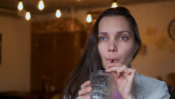 A Beautiful Woman in a Cafe Drinks a Cocktail From a Glass Glass with a Straw