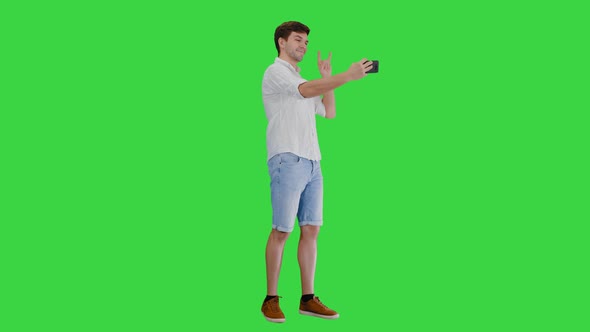 Young Man in Casual White Shirt Taking Selfies on His Phone on a Green Screen, Chroma Key.