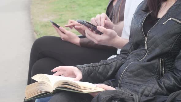 Friends Are Sitting on Bench in the Park in the Summer and Reading a Book