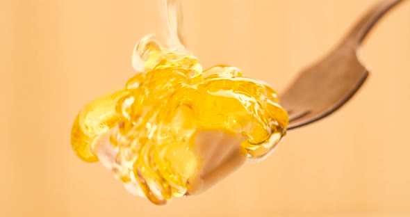 Liquid Organic Honey Dripping on a Fork with Cheese on a Light Background