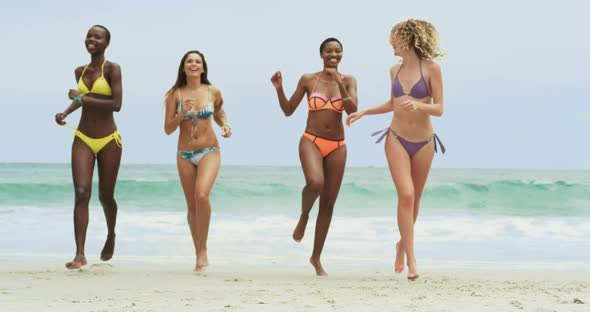 Front view of mixed-race female friends running on the beach 4k