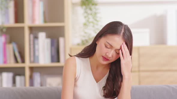 Asian woman sitting on sofa have a headache and Migraine feeling so stressed