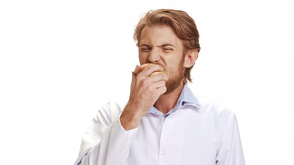 Strong Caucasian Young Doctor with Light Beard and Medical Overall Eating Apple Smiling on White