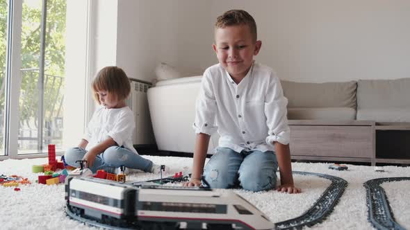 Two Children Playing with Toy Railroad Together at Home