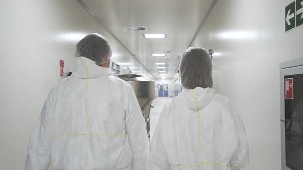 Following Back Shot of Two Factory Workers Walking Through Pharmaceutical Plant Hall