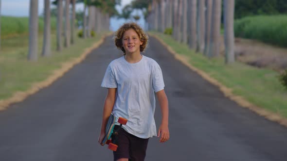 A Teenager with Long Hair Rides a Skateboard Along a Beautiful Road with Palm Trees