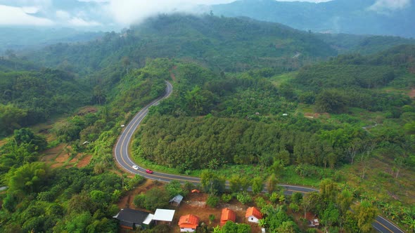 An aerial view of a winding road with moving cars in the tropical forests of Thailand. 4K