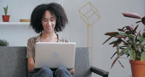 Young American Businesswoman Sits on Sofa at Home in Office, Works Remotely Online, Answers Emails