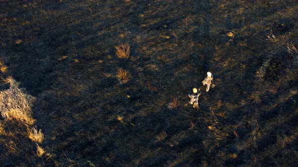 Two Firefighters Walk on Black Scorched Earth After Fire Dry Grass in a Field