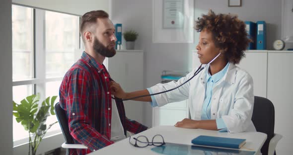 Female Doctor Examining Patient Heart Beat with Stethoscope in Office