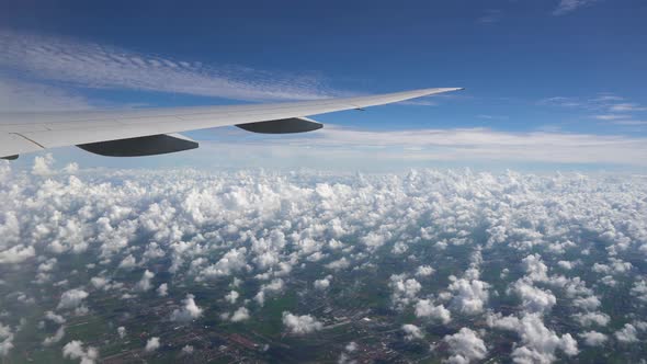 The Plane Flies in the Blue Sky. White Clouds and City Below Under the Wing of Aircraft