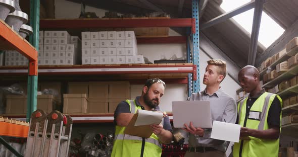 Two Caucasian and an African American male factory worker at a factory pointing, holding a clipboard