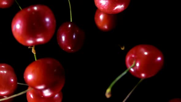 Close-up of Red Cherries Flying Up and Rotating on a Black Background