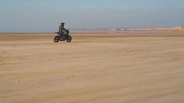 Motorcyclist Driving His Customized Fast Motorbike on the Dirt Road in Desert Around Sea or Lake