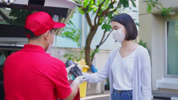 Asian deliver man wearing face mask in red uniform handling parcel box give to woman customer.