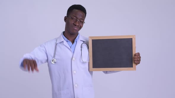Young Stressed African Man Doctor Holding Blackboard and Giving Thumbs Down