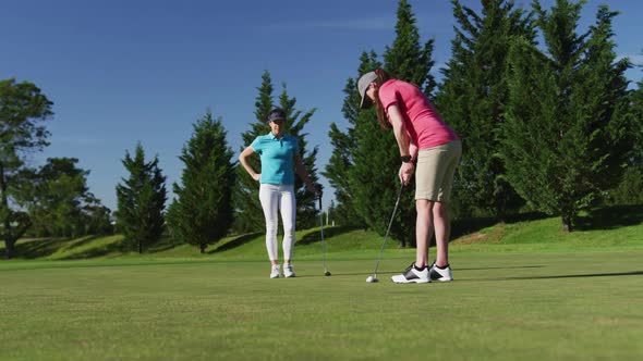 Two caucasian women playing golf one taking shot from bunker