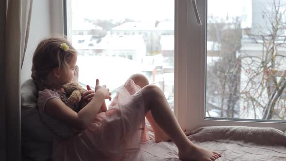 Child Girl Sits and Looks Sadly Out the Window