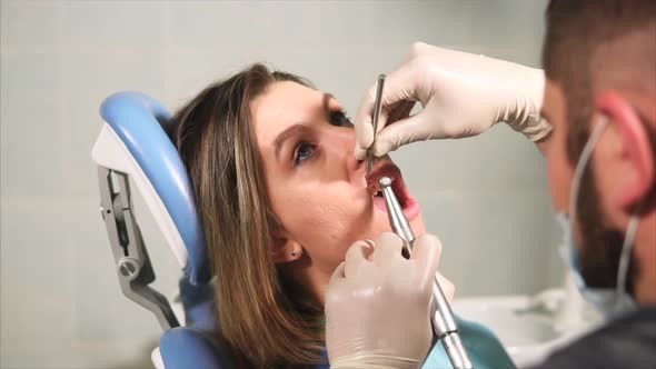 Doctor Dentist Cleans Teeth for Young Woman From Plaque and Tartar