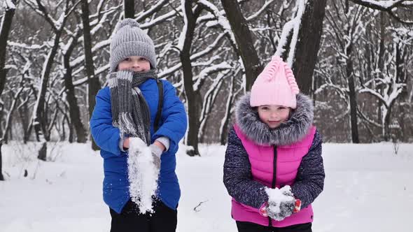 Children a Boy and a Girl in the Forest in Winter Jump Throw Snow and Laugh