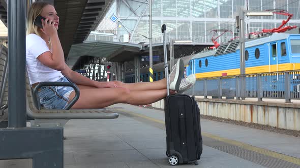 A Young Beautiful Woman Talks on a Smartphone on a Train Station Platform