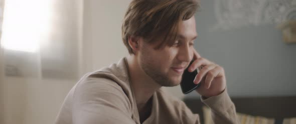 A man talking to someone on the phone while working with a laptop from home.