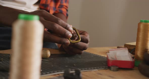 Close up of hands of african american craftsman preparing belt in leather workshop