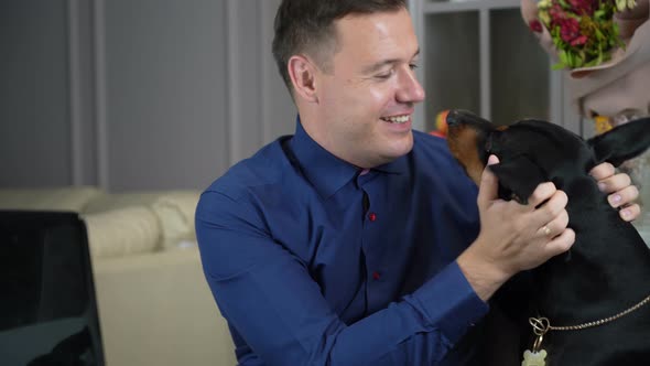 Millennial Man is Working From Home with His Computer in Office and His Dog Distracts Him