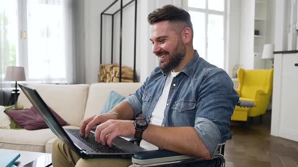 Bearded Young Guy in Casual Clothes which Sitting in Wheelchair at Home and Remotely Working