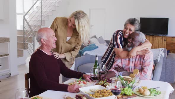 Diverse senior couples sitting by a table drinking wine eating dinner and hugging